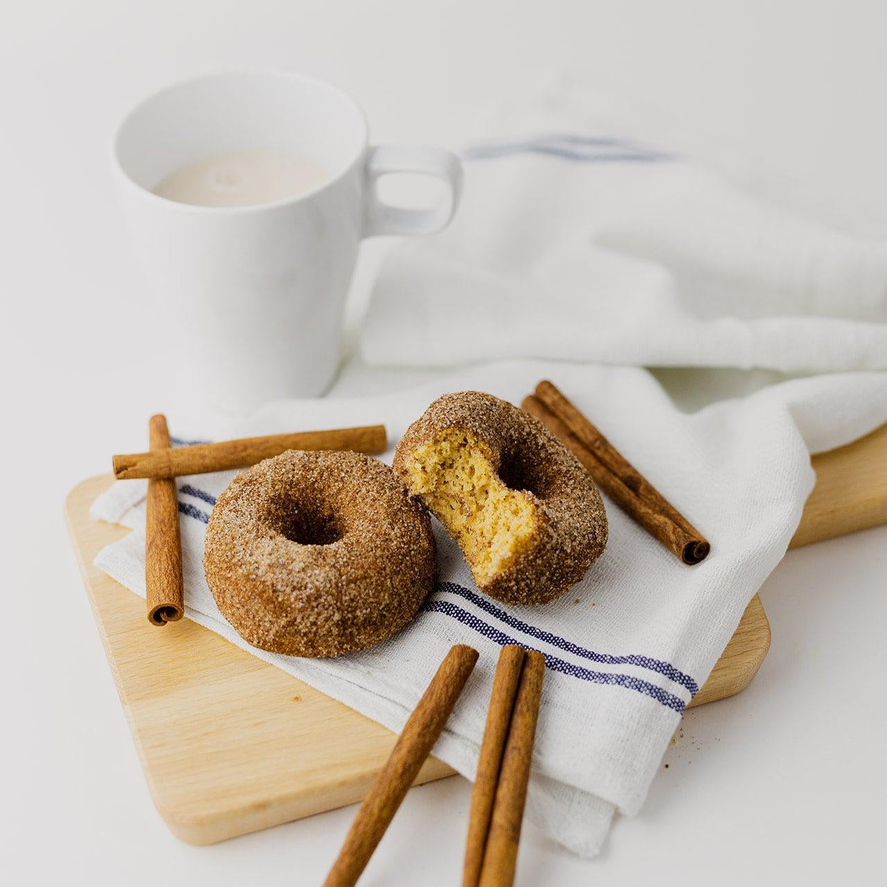 2 Cinnamon Sugar Donuts next to cinnamon sticks & a glass of milk