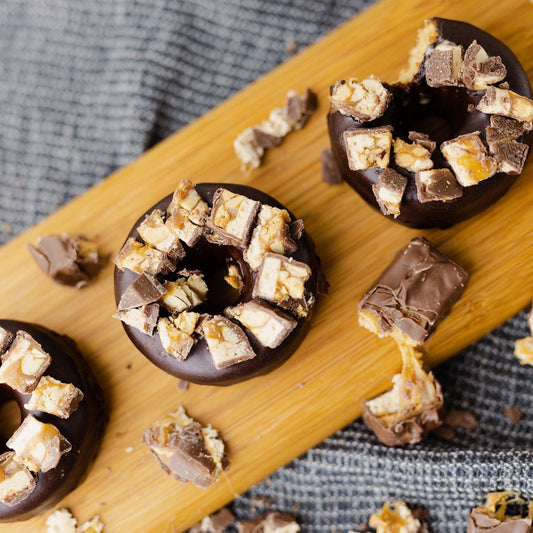 3 Snickers Protein Donuts on a long cutting board